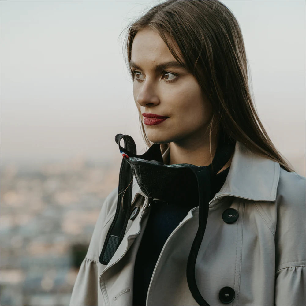Woman in a light trench coat with an R-PUR mask resting at her neck in the city, easy to pull up as a travel mask